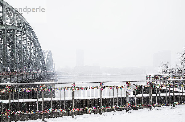 Vorhängeschlösser am Geländer der Hohenzollernbrücke über den Rhein gegen den Himmel bei Schneefall