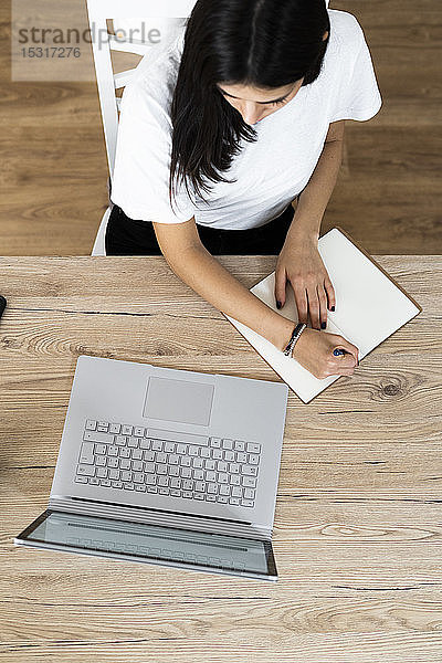 Draufsicht einer jungen Frau mit Laptop  die Notizen macht