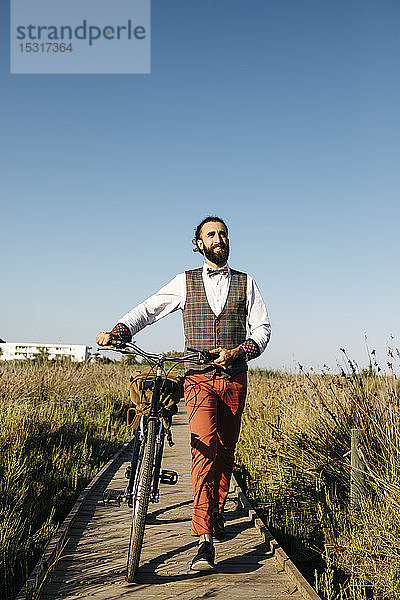 Gut gekleideter Mann  der nach der Arbeit mit dem Fahrrad auf einem Holzsteg auf dem Land unterwegs ist