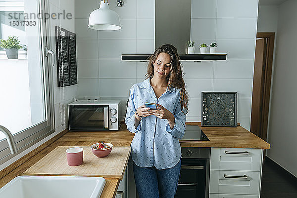 Junge Frau mit Pyjama in der Küche zu Hause am Handy