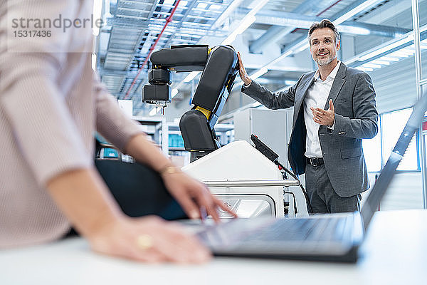 Geschäftsmann und Geschäftsfrau mit Laptop und Roboter in einer modernen Fabrikhalle
