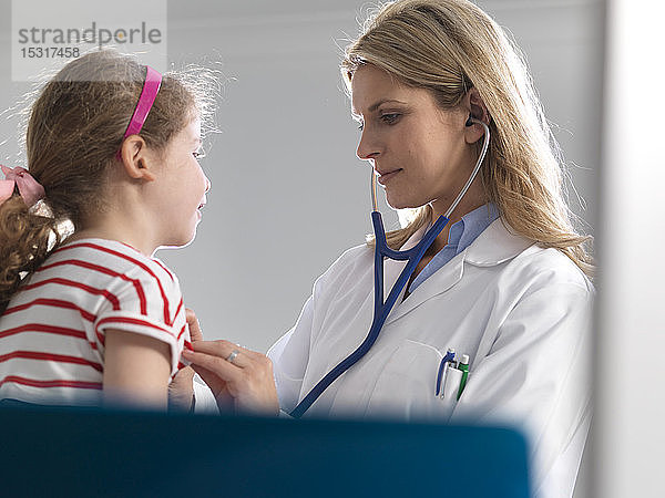 Ärztin  die in einer Klinik das Herz eines jungen Mädchens mit einem Stethoskop abhört