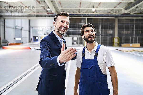 Glücklicher Geschäftsmann und Arbeiter in einer Fabrik