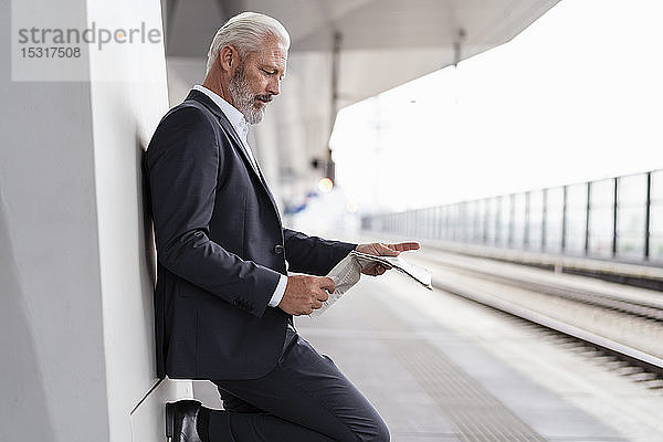Älterer Geschäftsmann liest Zeitung auf dem Bahnsteig