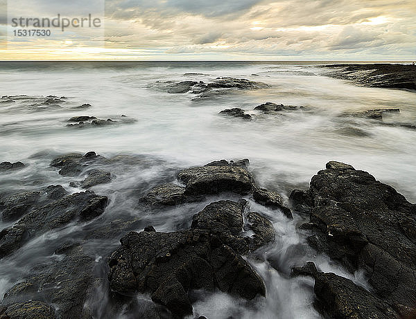 Vulkangestein inmitten von Wasser im Puuhonua O Honaunau National Historical Park vor bewölktem Himmel bei Sonnenuntergang