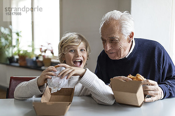 Glücklicher Grossvater und Enkel essen zu Hause gemeinsam Burger