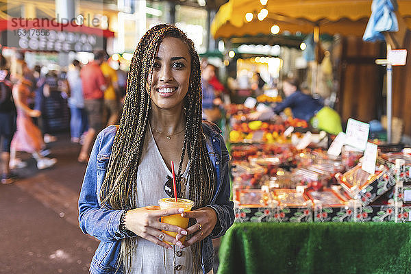 Porträt einer glücklichen jungen Frau mit frischem Orangensaft auf dem Straßenmarkt  London  UK