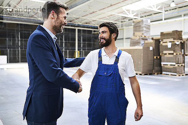 Geschäftsmann und Arbeiter beim Händeschütteln in einer Fabrik