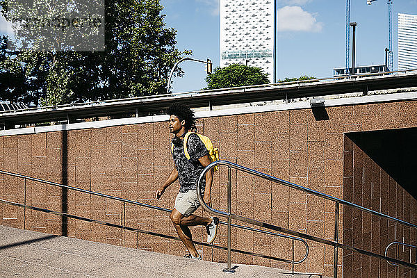 Mann mit gelbem Rucksack und Kopfhörern läuft die Treppe hinauf  Barcelona  Spanien