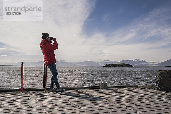 Junge Frau steht auf einem Steg und schaut durch ein Fernglas  Südost-Island