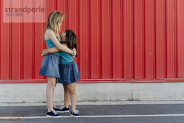 Schwestern umarmen sich vor einer roten Wand