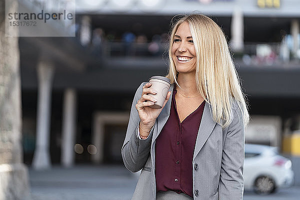 Porträt einer glücklichen blonden Geschäftsfrau mit Kaffee zum Mitnehmen