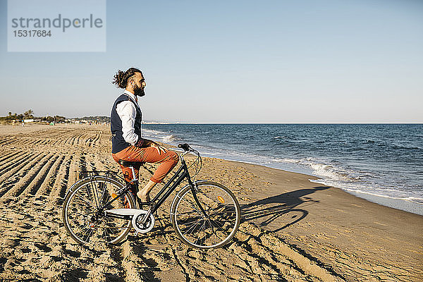 Gut gekleideter Mann mit seinem Fahrrad am Strand
