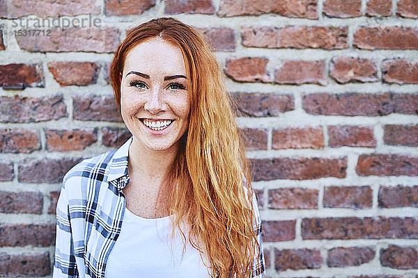 Porträt einer schönen jungen Frau  die vor einer Ziegelmauer vor der Kamera lächelt