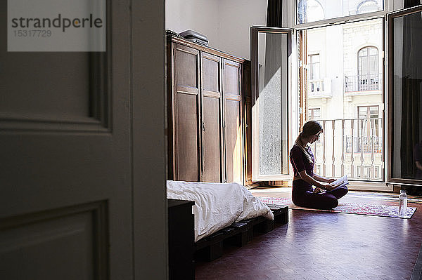 Junge brünette Frau praktiziert Yoga im Studentenwohnheim und liest ein Buch