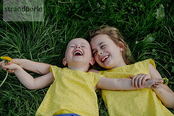 Zwei lachende Schwestern liegen auf einer Wiese und tragen gelbe Oberteile