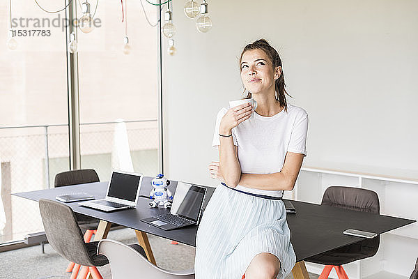 Junge Geschäftsfrau macht Kaffeepause im Büro und schaut auf