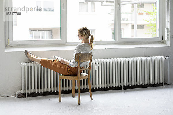 Junge Frau sitzt im Büro auf einem Stuhl am Fenster