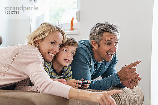 Glückliche Eltern mit Sohn spielen zu Hause auf der Couch Videospiele