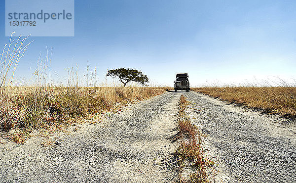 Geländewagen  der auf einer unbefestigten Straße in einer typisch afrikanischen Savannenlandschaft fährt  Makgadikgadi Pans  Botswana