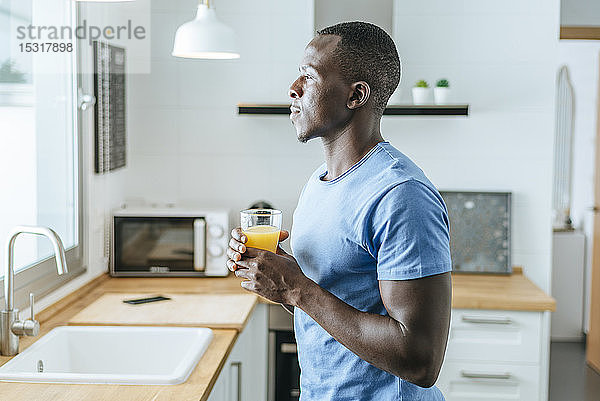 Junger Mann mit Orangensaft in der heimischen Küche