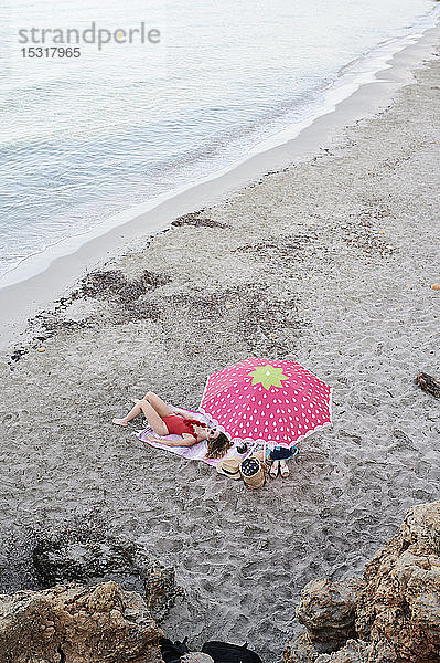 Junge Frau liegt auf einem Handtuch am Strand und sonnt sich