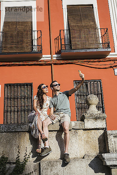 Paar  das auf einer Mauer sitzt und sich mit einem Smartphone selbstständig macht  Granada  Spanien