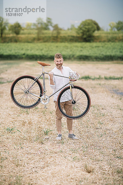 Mann mit handgefertigtem Rennrad auf Stoppelfeld