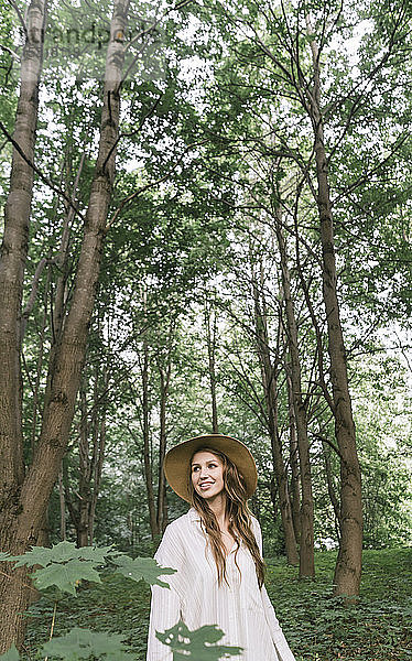 Lächelnde junge Frau mit Hut beim Waldspaziergang