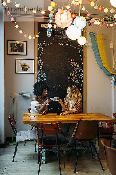 Multikulturelle Frauen unterhalten sich in einem Café und stoßen mit einer Tasse Kaffee an