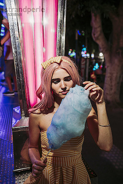 Porträt einer jungen Frau mit Zuckerwatte auf einem nächtlichen Rummelplatz