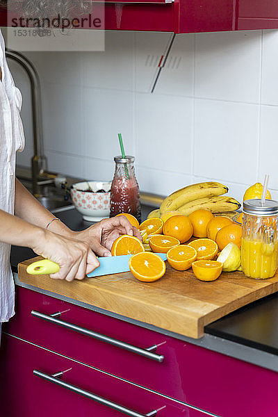 Nahaufnahme einer Frau in der Küche  die Orangen für einen Saft in Scheiben schneidet