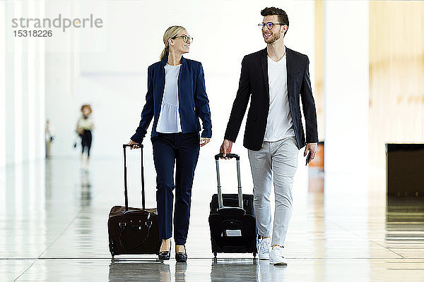 Zwei lächelnde junge Geschäftspartner beim Spaziergang am Flughafen