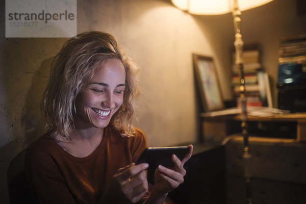 Porträt einer lachenden jungen Frau  die zu Hause ein Smartphone benutzt