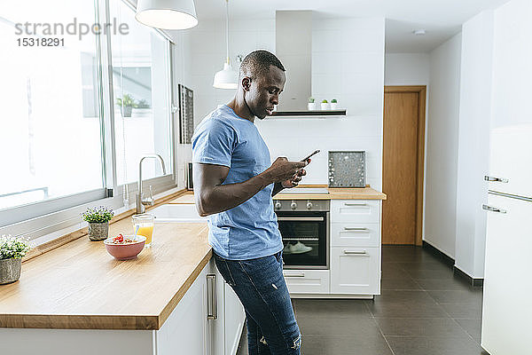 Junger Mann benutzt Handy in der Küche zu Hause