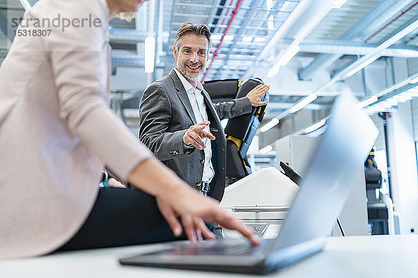 Geschäftsmann und Geschäftsfrau mit Laptop und Roboter in einer modernen Fabrikhalle