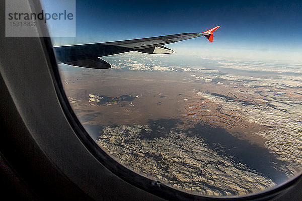 Flugzeugflügel über der Wüste durch Fenster gesehen