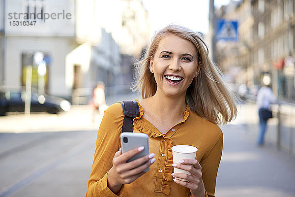 Porträt einer glücklichen jungen Frau mit Smartphone und Kaffee zum Mitnehmen in der Stadt