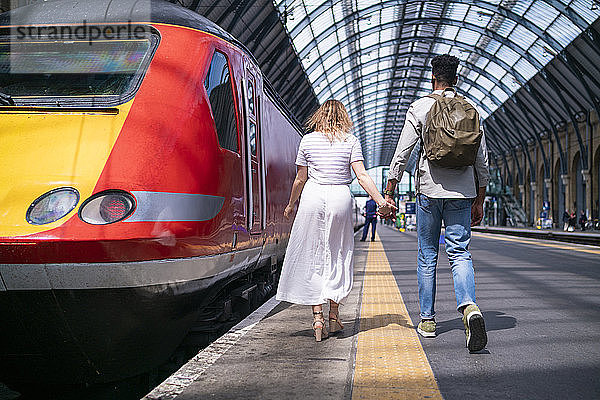 Rückenansicht eines jungen Paares  das Hand in Hand auf dem Bahnsteig geht  London  UK