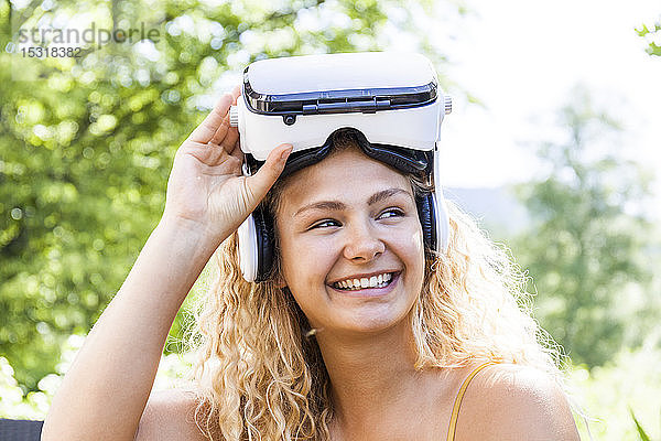 Junge blonde Frau  die im Freien eine Virtual-Reality-Brille trägt und zur Seite schaut