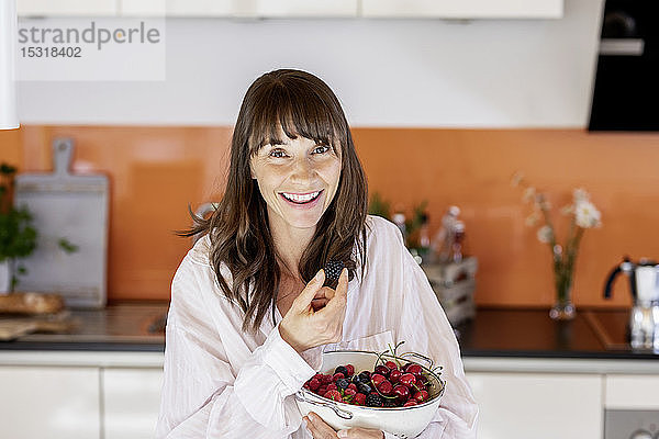 Porträt einer glücklichen Frau im Pyjama  die zu Hause in der Küche Obst isst