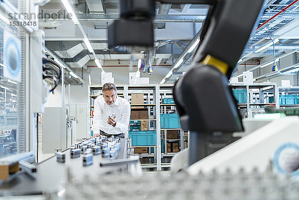 Geschäftsmann in einer modernen Fabrikhalle mit Blick auf Roboter