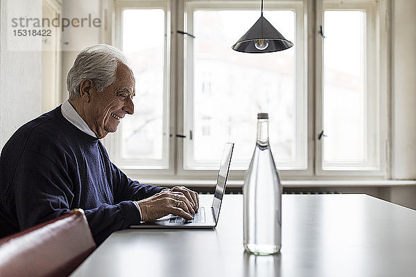 Lächelnder älterer Mann mit Laptop auf dem Tisch zu Hause