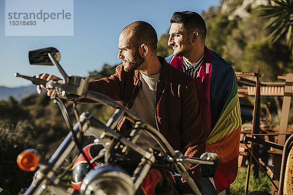 Schwules Paar mit schwuler Stolz-Fahne auf einem Motorrad