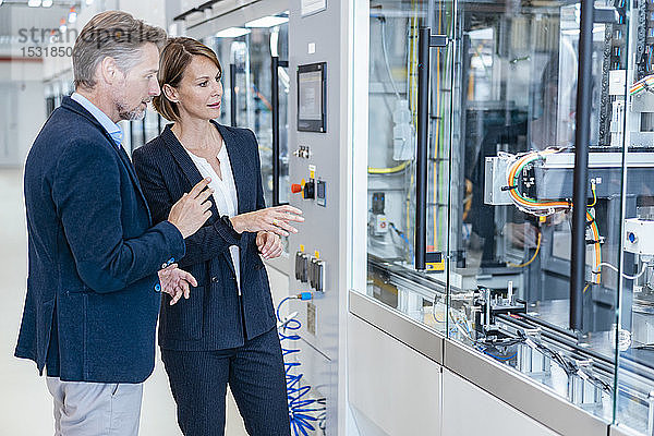 Geschäftsmann und Geschäftsfrau betrachten eine Maschine in einer modernen Fabrikhalle