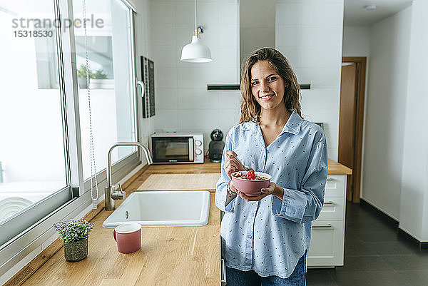 Porträt einer jungen Frau  die einen Pyjama trägt und zu Hause in der Küche Müsli isst