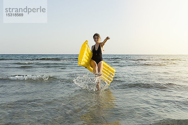 Junge Frau mit gelbem Luftbett am Strand