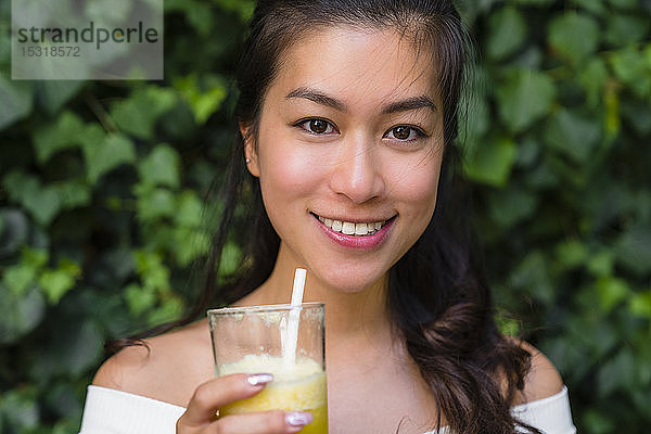Porträt einer lächelnden jungen Frau  die ein gesundes Getränk in der Hand hält
