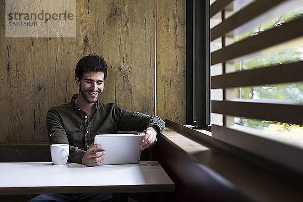 Porträt eines lächelnden Mannes mit digitalem Tablett in einem Cafe
