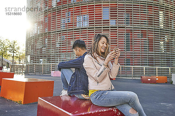 Paar sitzt Rücken an Rücken und benutzt Handys  Barcelona  Spanien